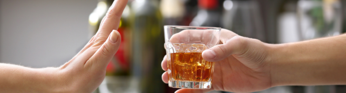 Man sieht eine Hand, die ein alkoholisches Getränk anbietet und eine Hand, die es ablehnt.